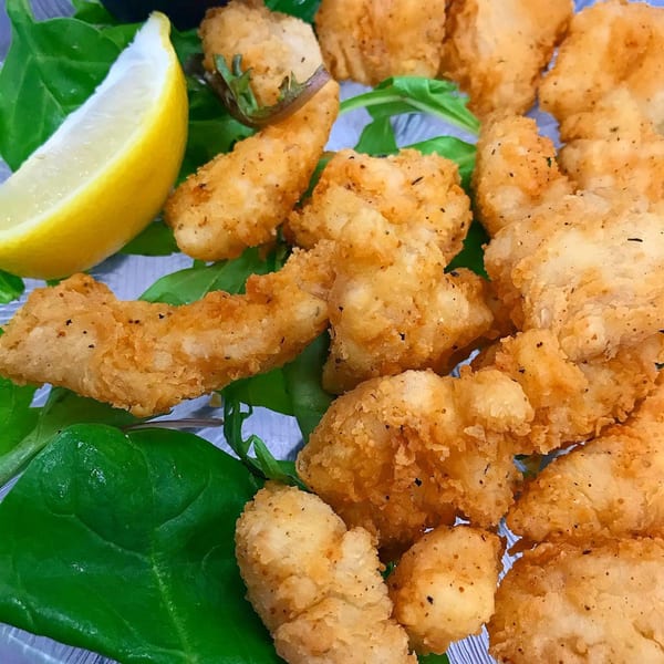 Golden fried seafood pieces, likely scallops or shrimp, with a lemon wedge and green garnish.