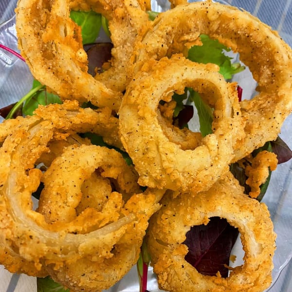 Golden-brown, crispy onion rings seasoned with pepper, served on a bed of fresh green and red lettuce.