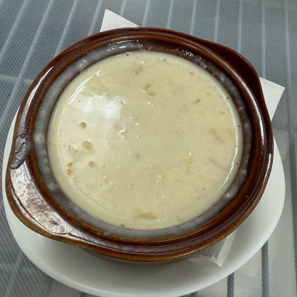 A brown bowl of creamy Sauder's Landing clam chowder on a white plate with a napkin.