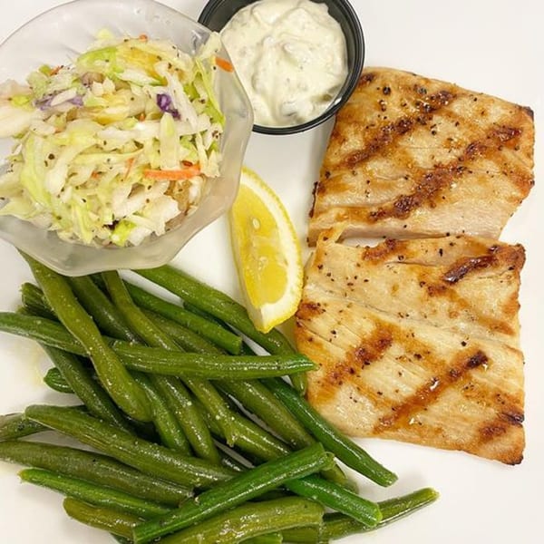 Grilled fish with green beans, coleslaw, tartar sauce, and a lemon wedge on a white plate.