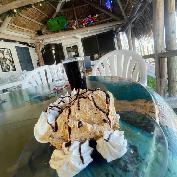 A slice of peanut butter pie with whipped cream and chocolate drizzle on a patio table.