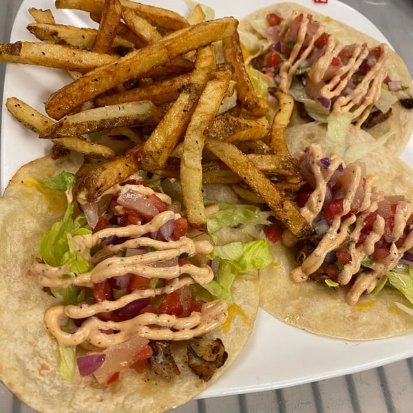 Two Sauder's Landing fish tacos with lettuce, pico de gallo, and sauce, served with fries.