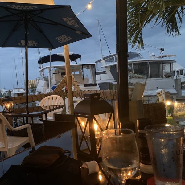 Outdoor dining table at Sauder's Landing with lanterns, drinks, and boats docked in the background.