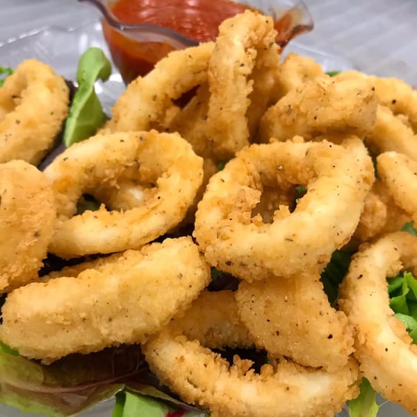 Crispy fried calamari rings with a side of red dipping sauce on a bed of fresh green lettuce.