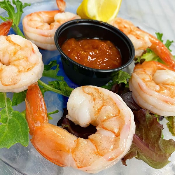 Sauder's Landing shrimp cocktail with sauce and lemon on a bed of lettuce and ice.