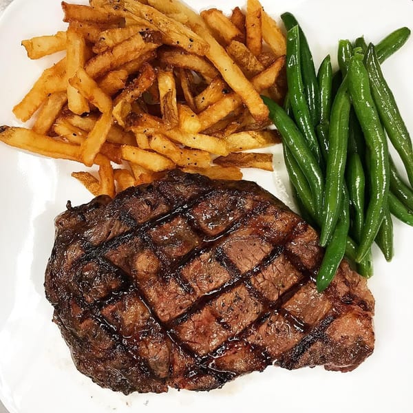 Grilled steak with crisscross grill marks, a pile of golden french fries, and vibrant green beans.